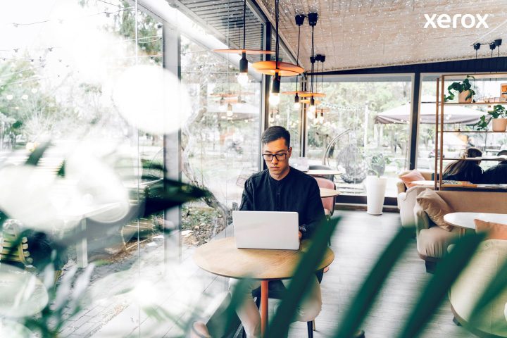 A man diligently working on his laptop in a bustling cafe, immersed in his tasks amidst a lively environment.