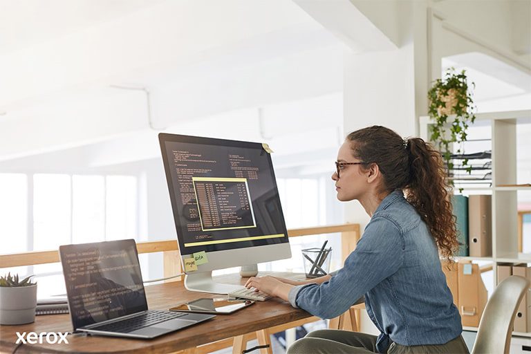 A woman at her desk, engaged with a computer and laptop, demonstrating productivity in a modern workspace.