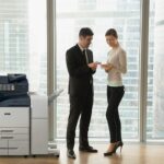 Two people in an office in business attire discussing documents stand by a Xerox® AltaLink® B8200 Series Multifunction Printer Two people in an office in business attire discussing documents stand by a Xerox® AltaLink® B8200 Series Multifunction Printer