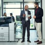 Two men in an office setting discussing something on a tablet beside a Xerox® AltaLink® C8200 Series Colour Multifunction Printer Two men in an office setting discussing something on a tablet beside a Xerox® AltaLink® C8200 Series Colour Multifunction Printer