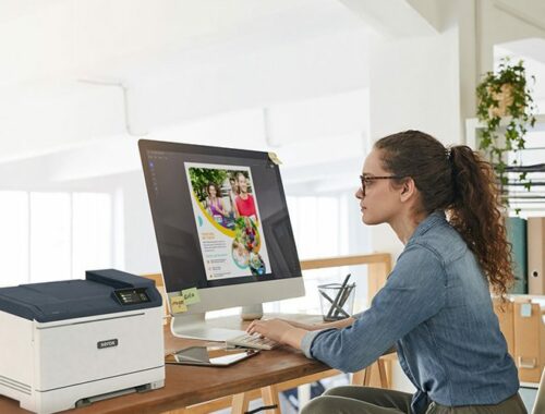 A woman seated at a desk, focused on her work, with a Xerox® C320 Colour Printer