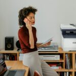 Xerox® C325 Colour Multifunction Printer in a home office environment A woman sitting at a desk having a call next to a Xerox® C325 Printer