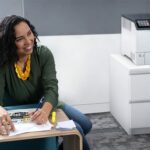 Xerox® VersaLink® C620 printer in an office Smiling woman in an office next to the Xerox® VersaLink® C620 Colour Printer